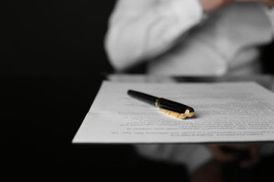 Photo of Notary sitting at black table, focus on fountain pen and document. Space for text