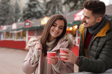 Photo of Young couple with cups of mulled wine at winter fair. Space for text