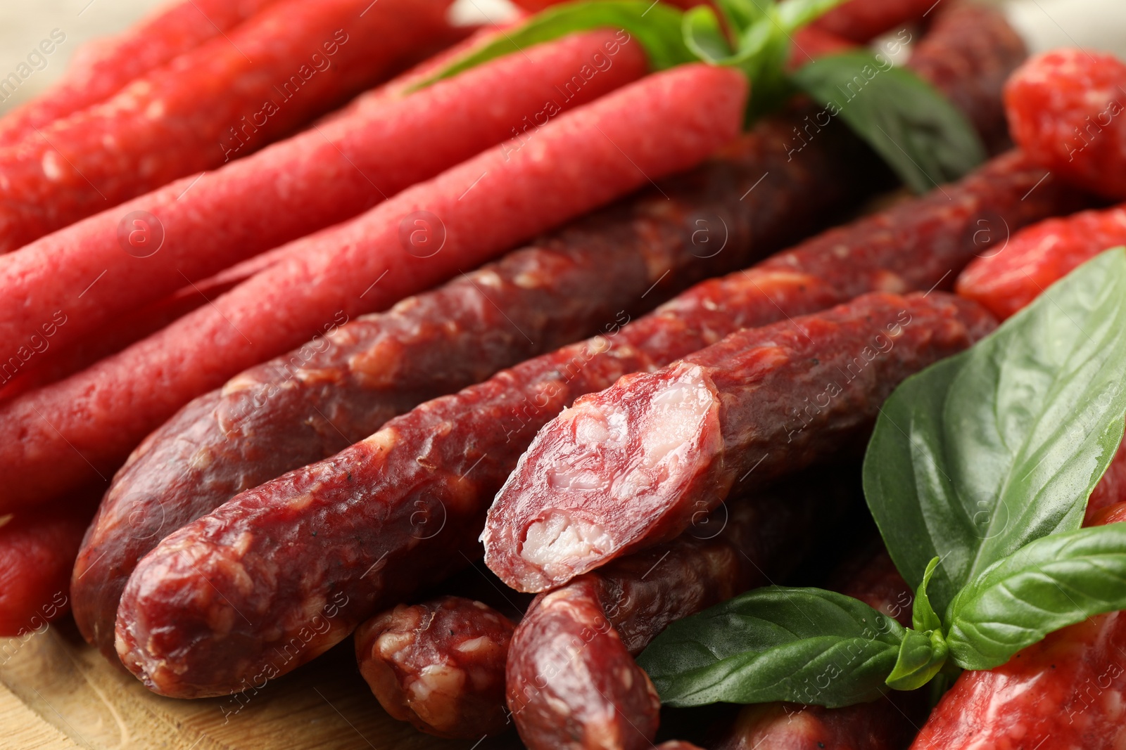 Photo of Different thin dry smoked sausages and basil on wooden table, closeup