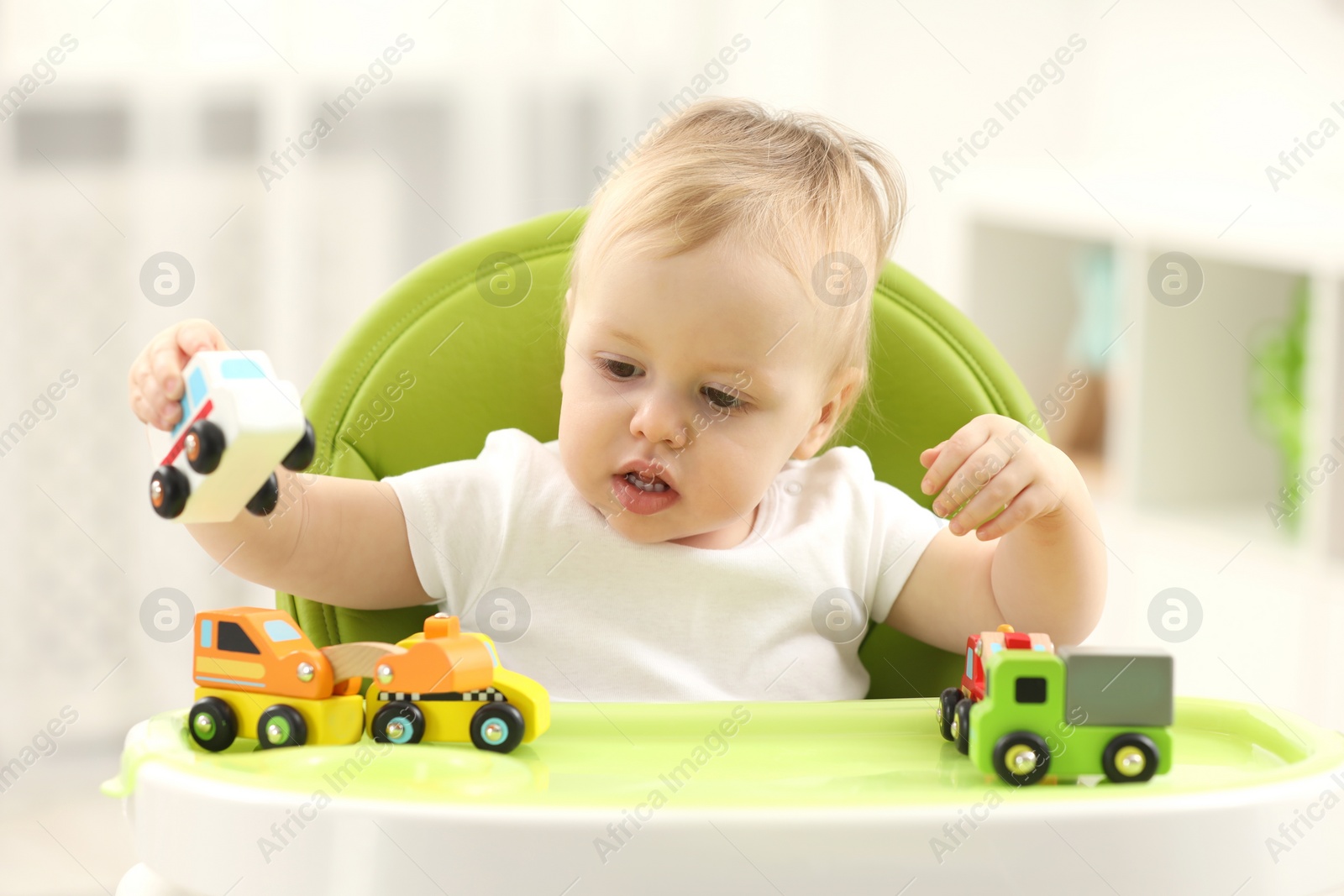 Photo of Children toys. Cute little boy playing with toy cars in high chair at home