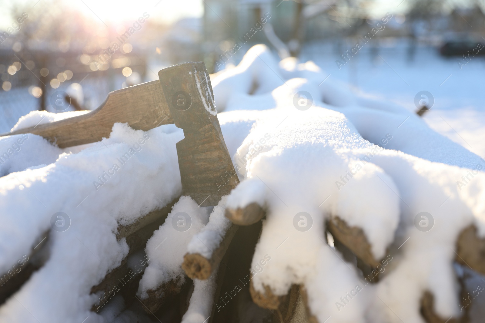 Photo of Metal axe on snowy firewood outdoors on sunny winter day