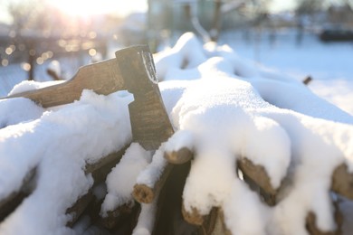 Metal axe on snowy firewood outdoors on sunny winter day