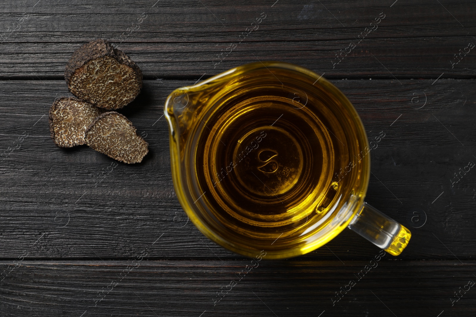 Photo of Fresh truffle oil in glass jug on black wooden table, flat lay