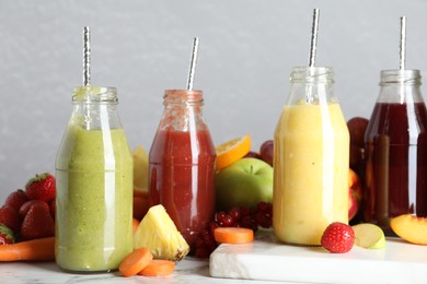 Bottles of delicious juices and fresh fruits on white marble table