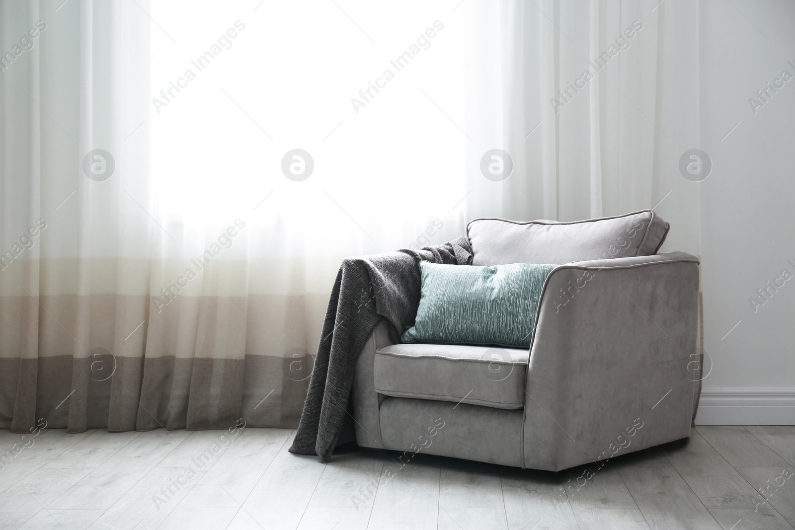 Photo of Cozy armchair with pillows and plaid near window in room. Interior design