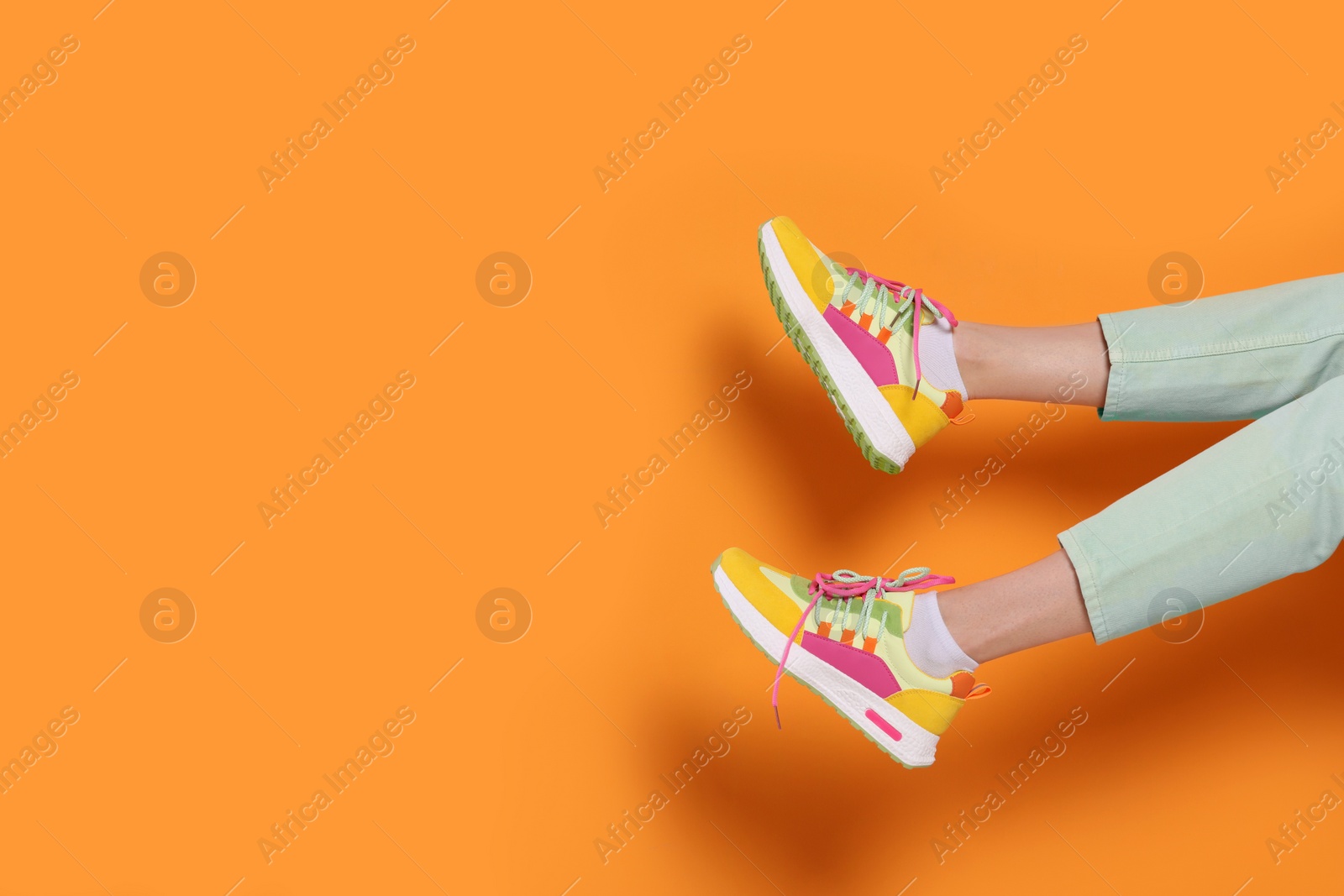 Photo of Woman wearing pair of new stylish sneakers on orange background, closeup. Space for text