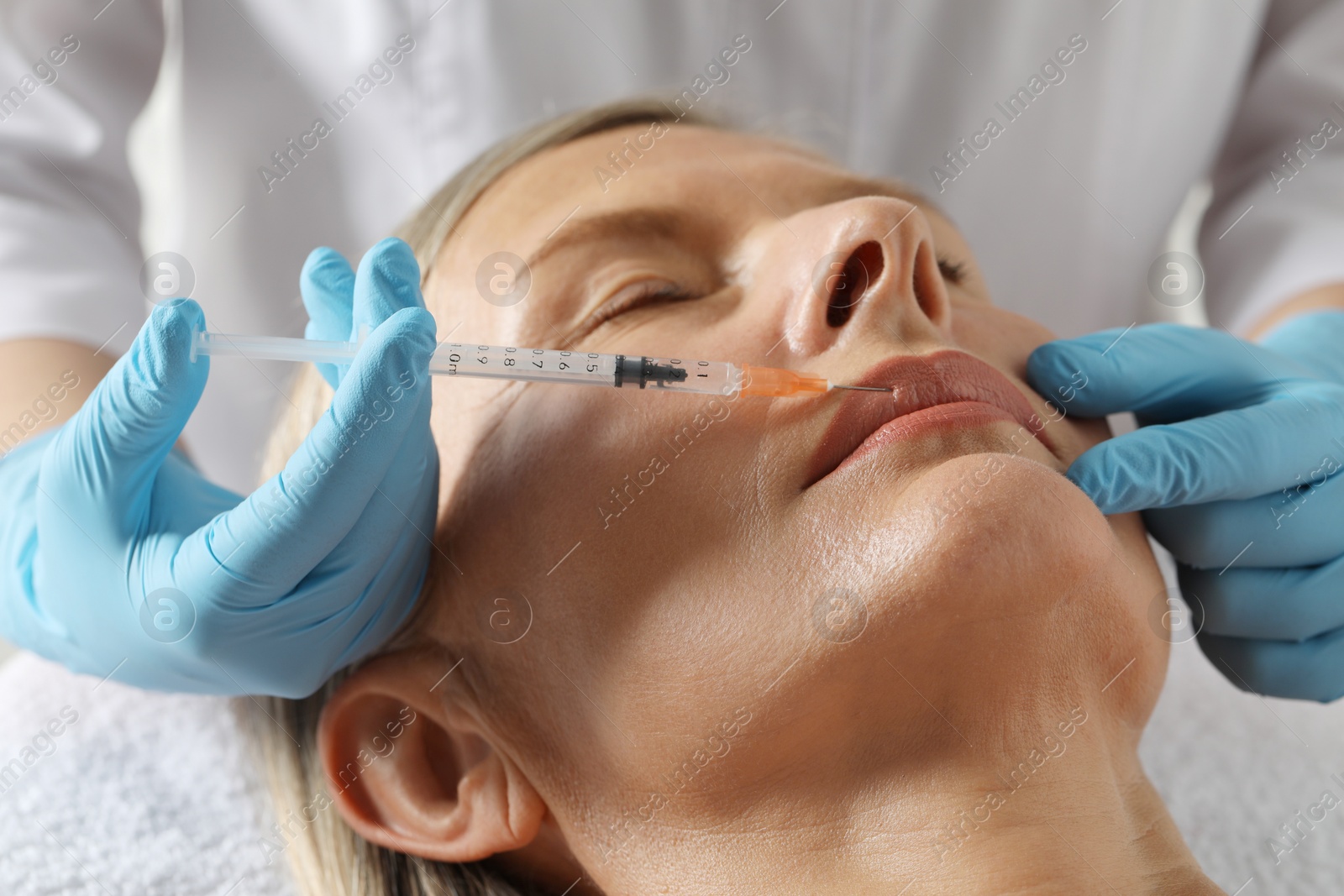 Photo of Doctor giving lips injection to senior woman in clinic, closeup. Cosmetic surgery