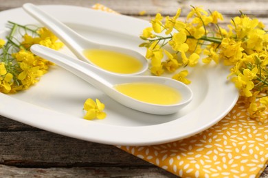 Photo of Rapeseed oil in gravy boats and beautiful yellow flowers on wooden table, closeup