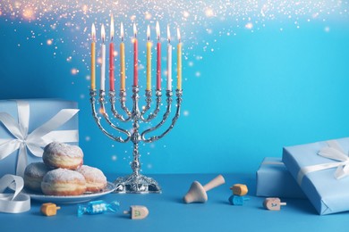 Hanukkah celebration. Menorah with burning candles, dreidels, donuts and gift boxes on light blue table, space for text