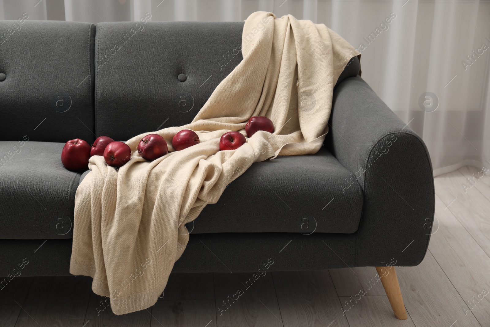Photo of Red apples and beige blanket on grey sofa indoors