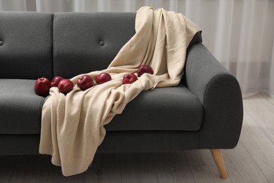 Photo of Red apples and beige blanket on grey sofa indoors