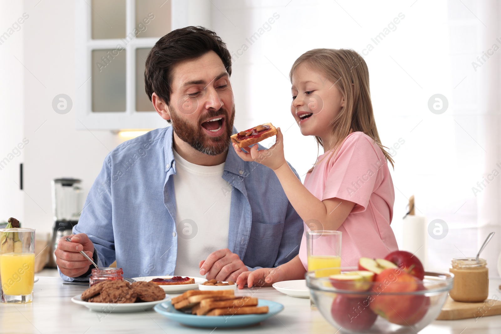 Photo of Father and his cute little daughter having fun during breakfast at table in kitchen