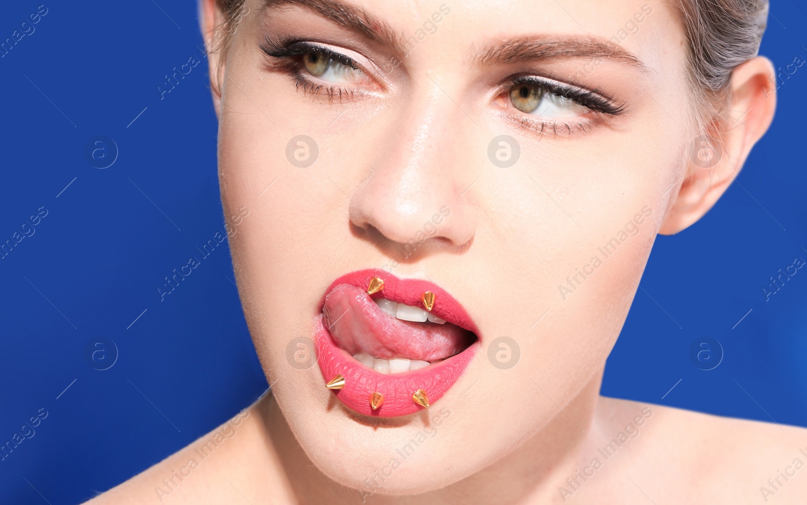 Photo of Beautiful young model with decorative spikes on lips against color background