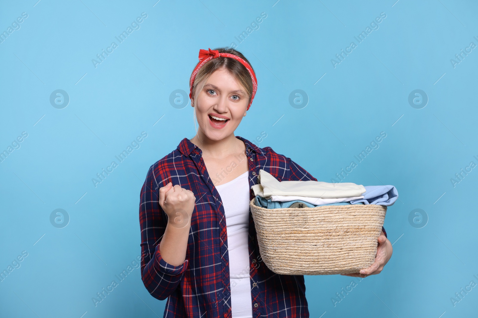 Photo of Emotional woman with basket full of laundry on light blue background