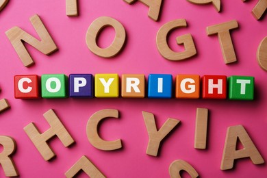 Photo of Colorful cubes with word Copyright and wooden letters on dark pink background, flat lay. Plagiarism concept