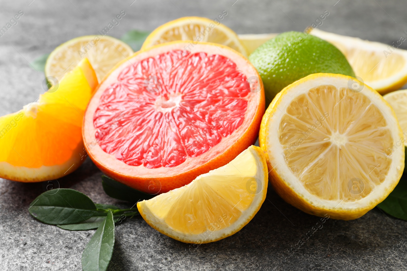 Photo of Different fresh citrus fruits and leaves on grey textured table, closeup