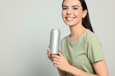 Beautiful happy woman holding beverage can on light grey background. Space for text