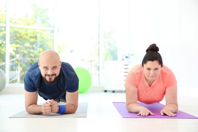 Overweight man and woman doing plank exercise on mats in gym