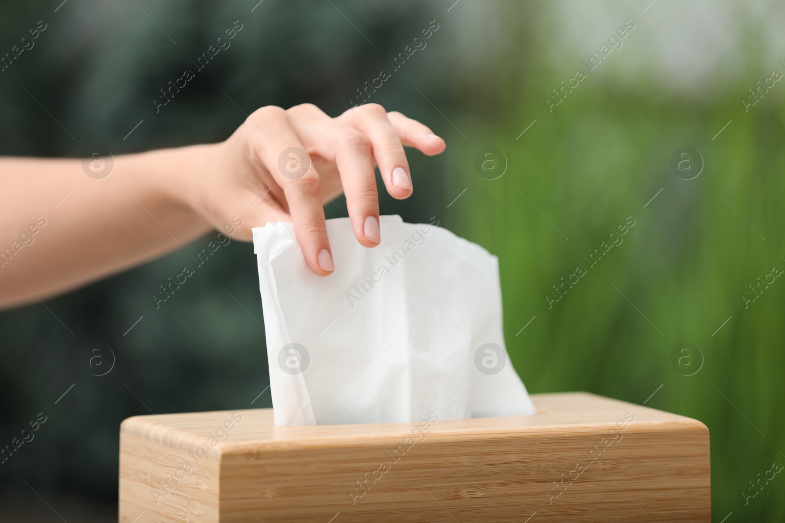 Photo of Woman taking paper tissue from holder on blurred background, closeup