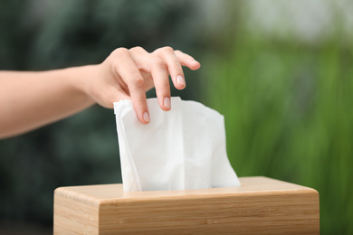 Woman taking paper tissue from holder on blurred background, closeup