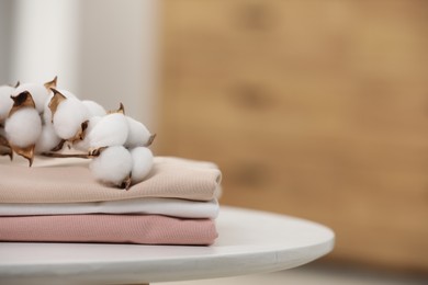 Bed sheets and cotton branch with fluffy flowers on white table in room, closeup. Space for text