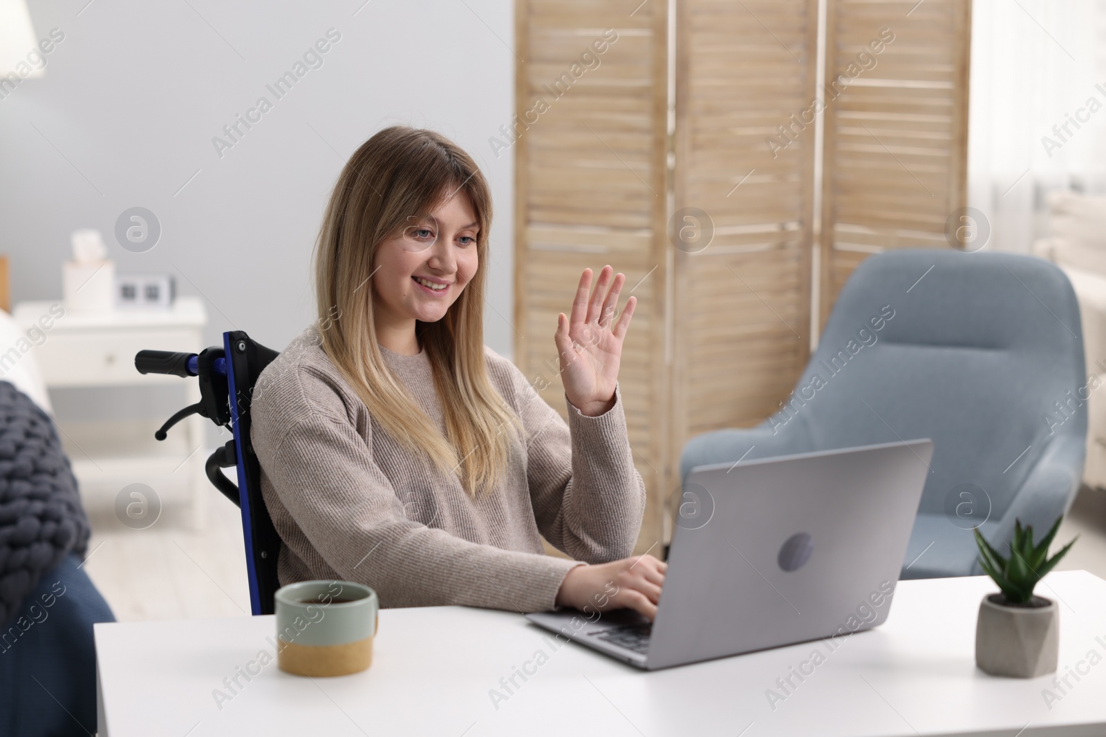 Photo of Woman in wheelchair having video chat via laptop at table in home office