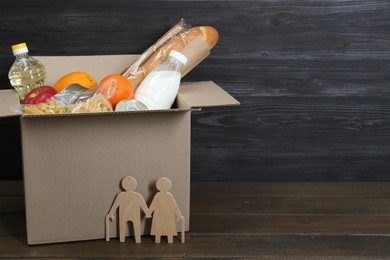 Humanitarian aid for elderly people. Cardboard box with donation food and figures of couple on wooden table, closeup