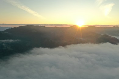 Aerial view of beautiful mountains covered with fluffy clouds at sunrise