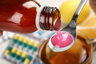 Photo of Pouring cough syrup from bottle into spoon on blurred background, closeup