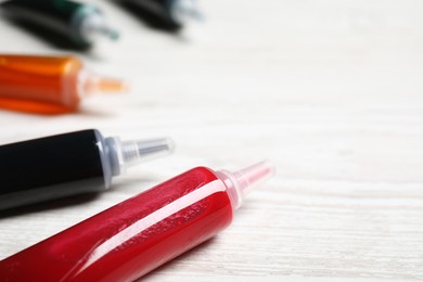 Tubes with different food coloring on white wooden table, closeup. Space for text