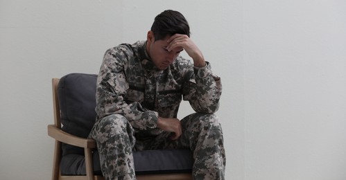 Stressed military officer sitting in armchair on white background