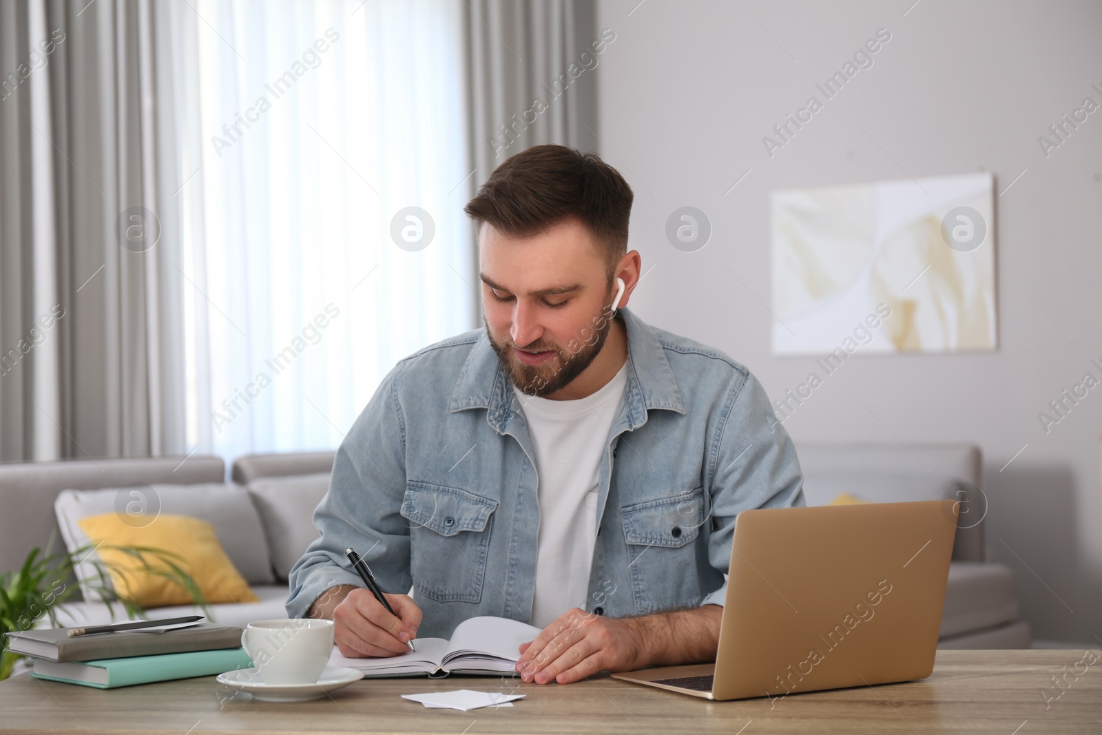 Photo of Young man taking notes during online webinar at table indoors