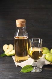 Photo of Delicious cider and apples with green leaves on black wooden table