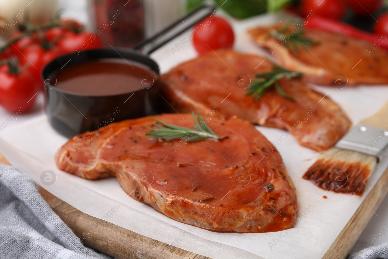 Photo of Raw marinated meat, rosemary and basting brush on table, closeup