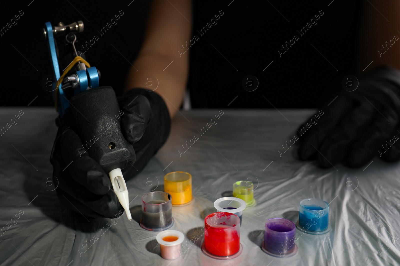 Photo of Tattoo artist with machine and inks at table, closeup