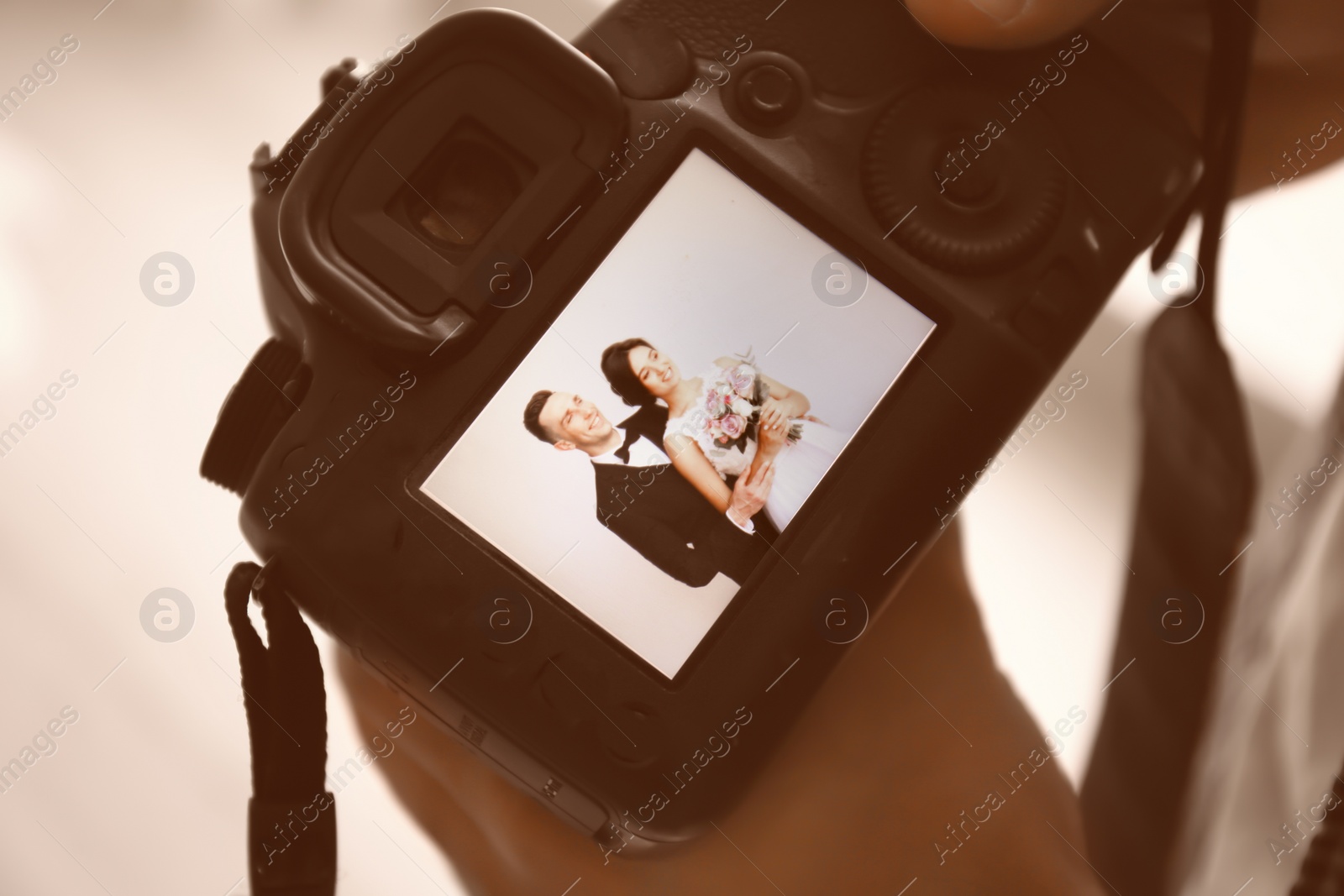 Photo of Professional photographer holding camera with lovely wedding couple on display, closeup