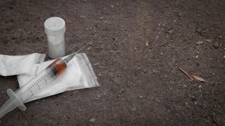 Plastic bags, container with powder and syringe on asphalt, space for text. Hard drugs