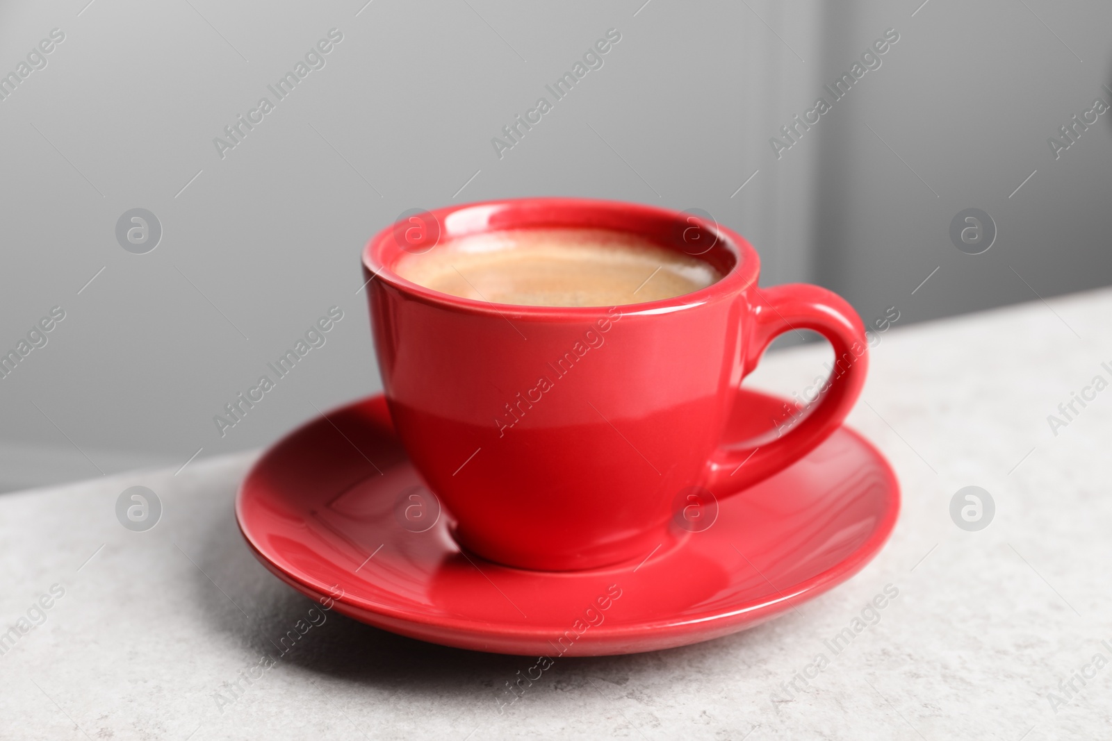 Photo of Red ceramic cup with hot aromatic coffee on white table indoors, closeup