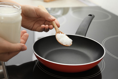 Woman cooking with coconut oil on induction stove, closeup