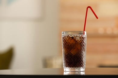 Glass of cola with ice on table against blurred background. Space for text