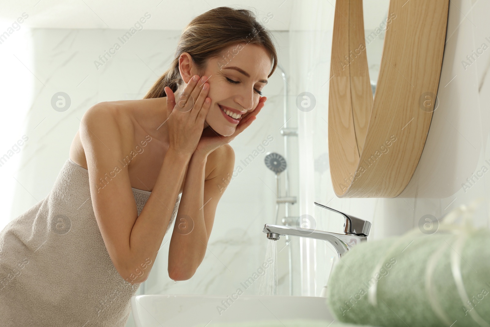 Photo of Young woman washing her face with water in bathroom