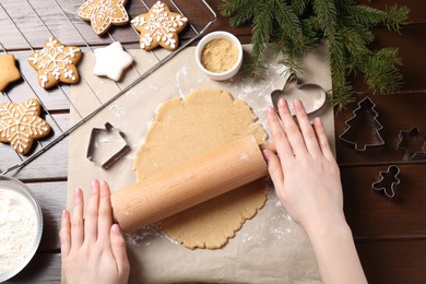 Making Christmas cookies. Woman rolling raw dough at wooden table, top view