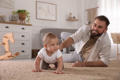 Photo of Happy young father helping his cute baby to crawl on floor at home