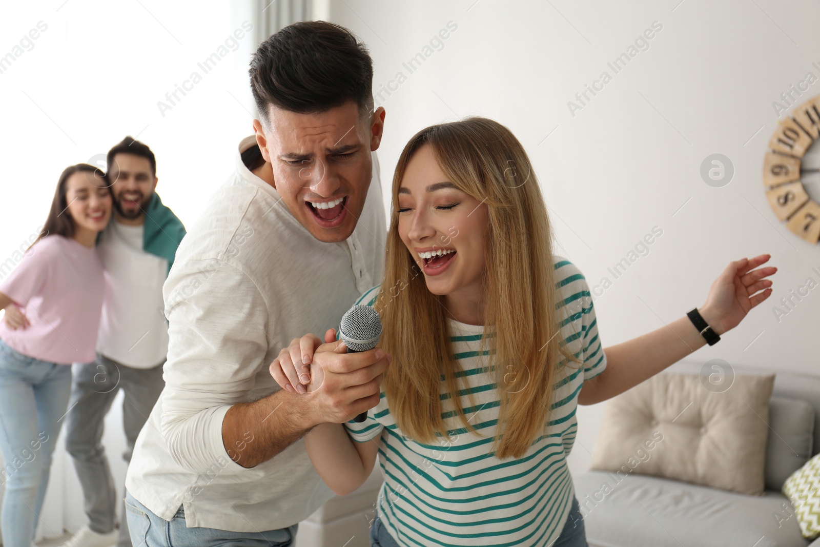 Photo of Happy couple singing karaoke with friends at home