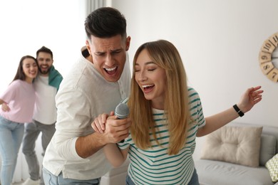 Photo of Happy couple singing karaoke with friends at home