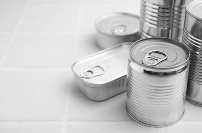 Photo of Many closed tin cans on white tiled table, closeup. Space for text