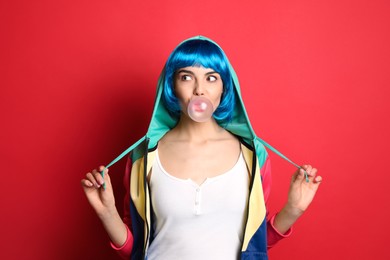 Photo of Fashionable young woman in colorful wig blowing bubblegum on red background