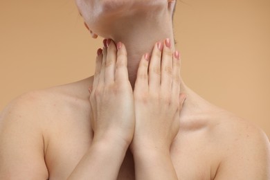 Woman touching her neck on beige background, closeup