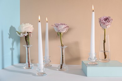 Photo of Elegant candlesticks with burning candles and flowers on white table
