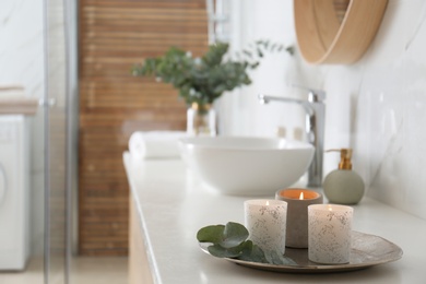 Photo of Tray with eucalyptus leaves and burning candles on countertop in bathroom